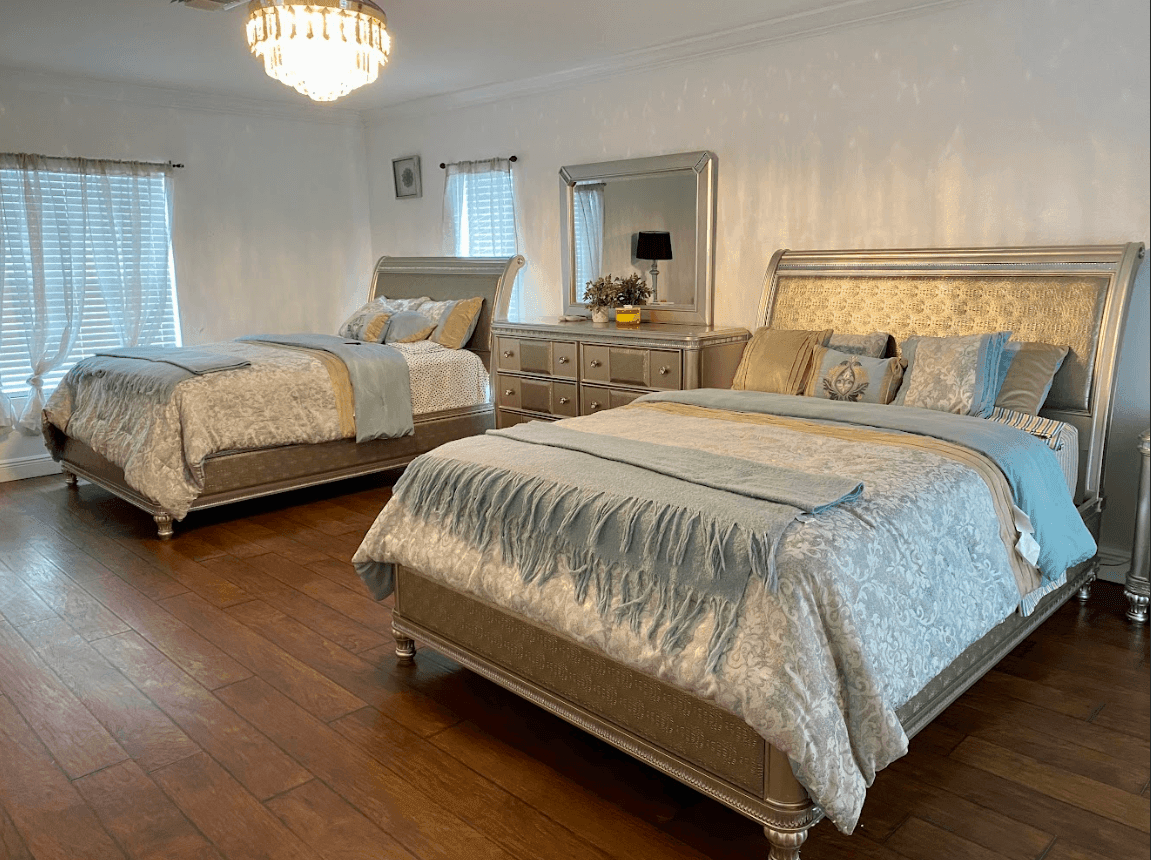 Elegant bedroom with two queen beds, mirrored dresser, and chandelier lighting.