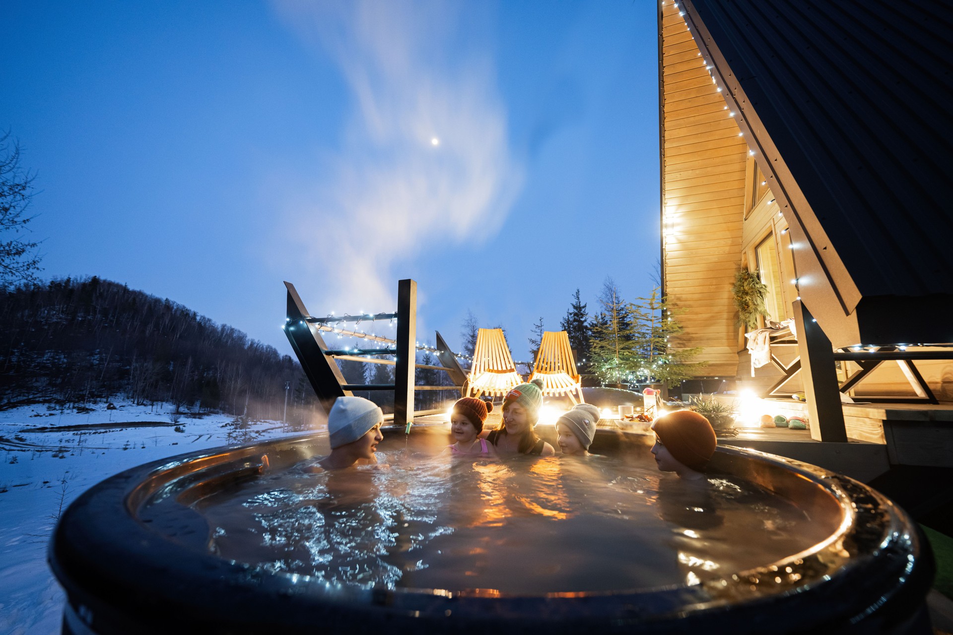 Family enjoying bathing in wooden barrel hot tub in the terrace of the cottage. Scandinavian bathtub with a fireplace to burn wood and heat water.